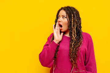 shocked plump african american woman is surprised and covers her mouth with her hand on a yellow...