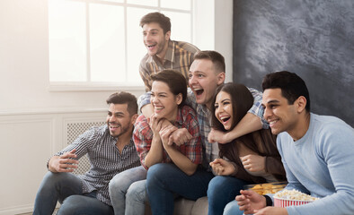 Happy friends with popcorn watch film on the sofa at home