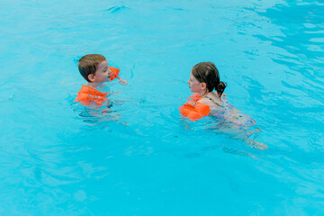 children are swimming in a pool wearing orange armbands.