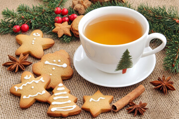 Fototapeta premium A cozy Christmas tea setup featuring a warm cup of tea surrounded by holiday gingerbread cookies in festive shapes, such as stars and trees.