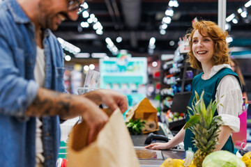 Customer packing groceries at checkout counter with smiling cashier