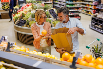 Senior couple choosing oranges in supermarket fruit section