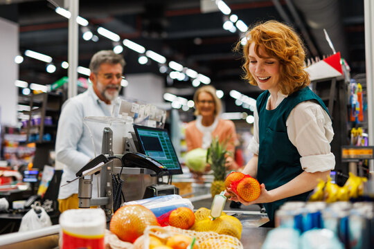 Cashier scanning groceries at supermarket checkout with customers waiting