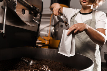 Filling coffee grains in a craft bag. Packing fried coffee beans. Worker pouring roasted coffee beans in packaging bag.