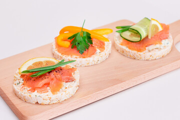 Rice Cake Sandwiches with Fresh Salmon, Cucumber, Yellow Paprika and Greens on Wooden Cutting Board. Diet Food. Quick and Healthy Sandwiches. Crispbread with Fresh Fillings. Healthy Dietary Snacks