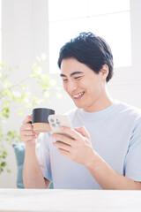 Handsome man with a drink in a brightly lit room, tapping, searching and operating a smartphone Vertical