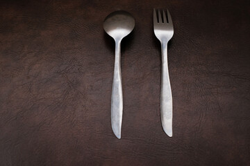 Fork and spoon stainless isolated on brown background, top view, eating place setting.