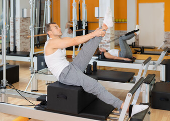 Man athlete works out in gym and performs set of exercises to stretch leg muscles with help of...