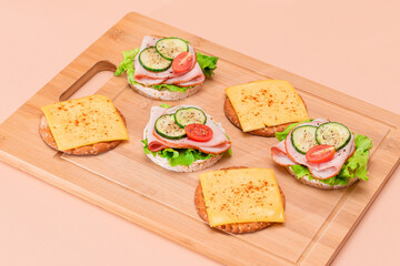 Light Breakfast. Quick and Healthy Sandwiches. Rice Cakes with Ham, Tomato, Fresh Cucumber, Green Salad and Cheese on Wooden Cutting Board. Beige Background