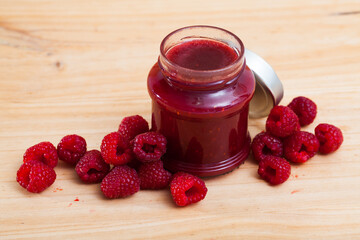 Close up of glass jar of raspberry jam and scattered fresh berries