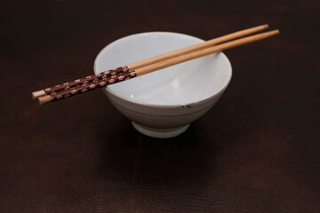 White bowl with wooden chopsticks on brown background, traditional wooden sticks for asian food.