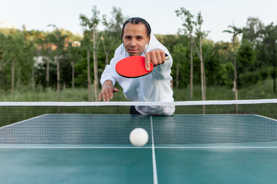 young african american guy playing table tennis outdoors in the park, a man hits the ball with a ping pong racket - Powered by Adobe