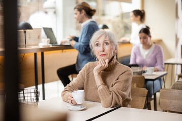 Sad elderly woman drinking coffee or tea at the bar counter alone