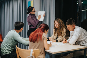 A group of students attentively listening and taking notes during a classroom session, guided by their teacher. The atmosphere is focused and collaborative, promoting active learning and discussion.