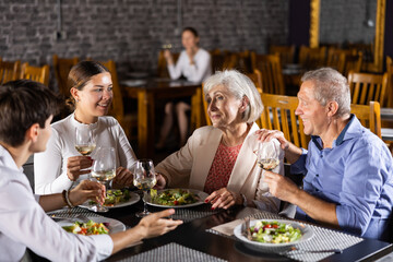 Elderly couple and young couple have dinner and drink wine together in restaurant