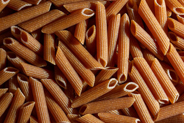 Uncooked Whole Grain Penne Rigate Pasta: A Culinary Canvas of Whole Wheat Macaroni, Creating a Lively and Textured Background for Gourmet Cooking. Whole Grain Dry Pasta. Whole Wheat Raw Macaroni