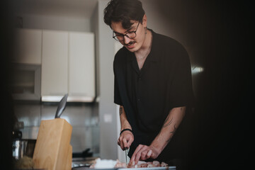A young man is engaged in cooking in a modern kitchen, demonstrating focus and precision while chopping ingredients. The setting is stylish and contemporary, emphasizing a passion for culinary arts.