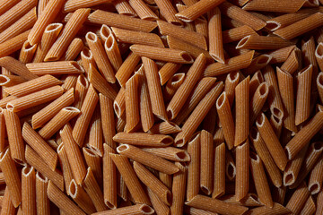 Uncooked Whole Grain Penne Rigate Pasta: A Culinary Canvas of Whole Wheat Macaroni, Creating a Lively and Textured Background for Gourmet Cooking. Whole Grain Dry Pasta. Whole Wheat Raw Macaroni
