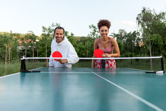 young cheerful african american couple playing table tennis outdoors in the park, woman and man competing as a couple in ping pong and having active rest