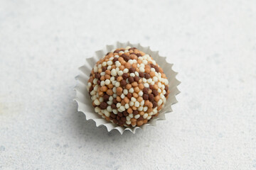 Typical Brazilian sweet brigadeiro. One candy with sprinkles on a white background