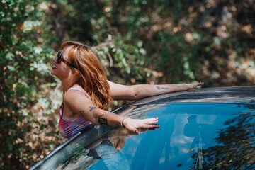 A cheerful woman leans out of a car sunroof, joyfully embracing freedom and adventure in a lush...