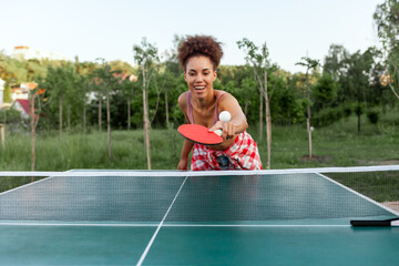 young african american girl playing table tennis outdoors in the park, woman hitting the ball with...