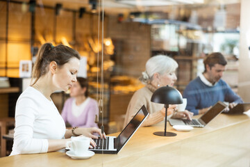Positive European businesswoman drinking and enjoying coffee while working on laptop in cafe. Freelance and remote work