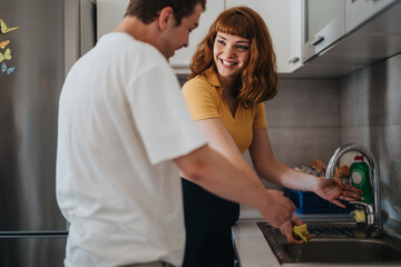 Obraz premium Happy couple washing dishes together in a modern kitchen. They are smiling and enjoying teamwork in their daily chores, creating a warm and cooperative atmosphere at home.