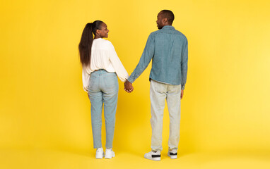 Black Couple Holding Hands Standing Back To Camera Posing Over Yellow Background. Studio Shot Of Unrecognizable African American Spouses. Marriage And Love Concept. Full Length