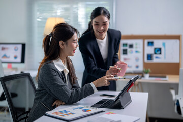 Two women in business attire are smiling and pointing at a computer screen