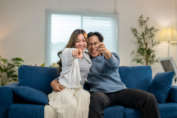 A couple is sitting on a blue couch, pointing at something