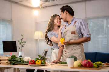 A man and woman are in a kitchen, holding a pepper and smiling at each other