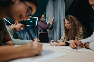 A group of students writing notes during a collaborative study session in a classroom setting. The...