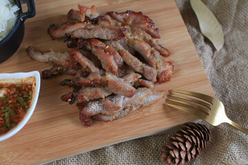 Grilled pork with dipping spicy sauce and sticky rice on wooden cutting board. Local street Thailand food. 