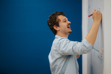 A young teacher engages with students as he writes on a whiteboard, passionately explaining concepts. The vibrant classroom setting inspires learning and knowledge sharing.