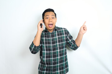 Fototapeta premium surprised asian man pointing hand while talking on smartphone isolated on white background, male wear casual green shirt