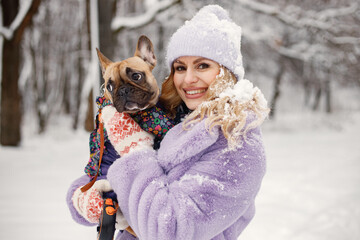 Woman in knitted hat playing with her dog french bulldog on a snow