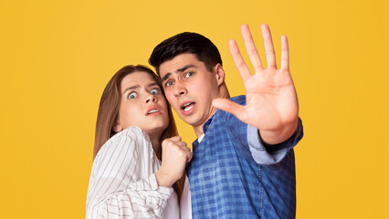 Guy protects frightened woman isolated on yellow background