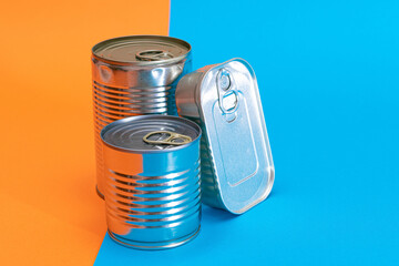 A Group of Stacked Tin Cans with Blank Edges on Split Blue and Orange Background. Canned Food. Different Aluminum Cans for Safe and Long Term Storage of Food. Steel Sealed Food Storage Containers