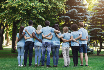 Volunteering, people and ecology concept. Group of volunteers embracing in park, back view, copy...
