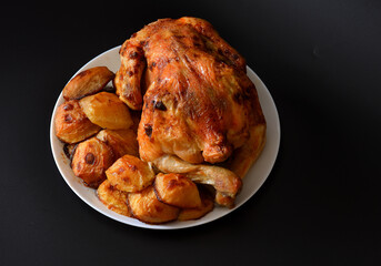Whole baked chicken with new potatoes on a large ceramic white plate.