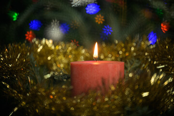Red Christmas candle burning, surrounded by a wreath and colorful snowflake bokeh highlights