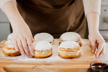 Woman prepares fresh donuts with jam in home kitchen. Cooking traditional Jewish Hanukkah sufganiyot.