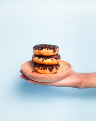 Stack of Donuts on a wooden plate. It's holding with hand on a blue background