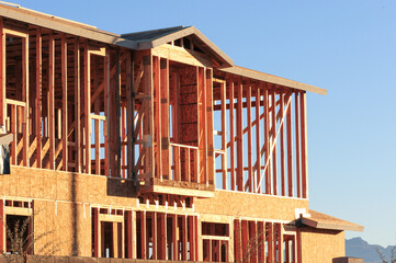 Exterior view of wood framing and structural components on a two-story house under construction, illustrating early-phase residential building with exposed studs, sheathing, and architectural design