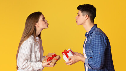 Man and woman making blow kiss and gives gifts, profile, free space, yellow studio background