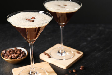 Glasses of delicious espresso martini and coffee beans on dark textured table, closeup