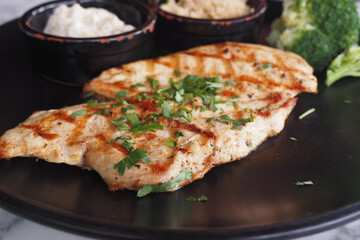 Delicious Grilled Chicken Fillet Accompanied by Broccoli and Savory Sauces on Black Plate