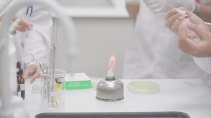 A group of people are gathered around a table with a Bunsen burner on it. They are wearing lab coats and gloves