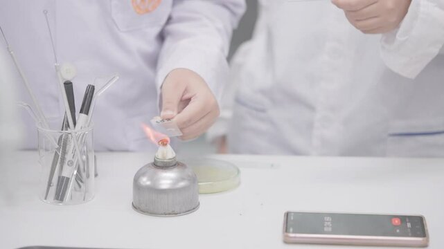 Two people are holding a lit candle and a cell phone. Scene is serious and focused, as the people are likely conducting an experiment or working on a project
